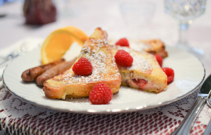 Stuffed french toast is topped with fresh raspberries and powdered sugar.
