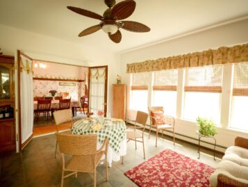 The sunroom shows antique furnishings, a small seating area, and a couch.