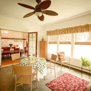 The sunroom shows antique furnishings, a small seating area, and a couch.